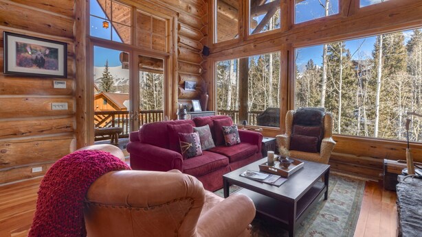 A log cabin interior with a large window, a sofa, a chair, and a table.