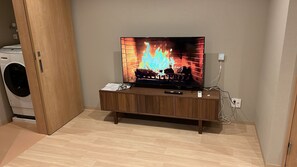 A living room with a television displaying a fireplace, a washing machine, and a wooden cabinet. - Tamatsukan/ JR Tsuruhashi 8 mins/ Early Check in (Osaka)
