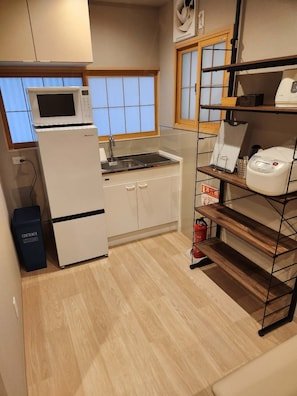 A compact kitchen with a microwave, sink, and white cabinets. There is a small trash bin and a shelf with kitchen appliances. - Tamatsukan/ JR Tsuruhashi 8 mins/ Early Check in (Osaka)