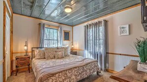 A bedroom with a bed, wooden nightstands, a desk, a potted plant, and a window with curtains. - Pet Friendly Creekside Cabin + Hot Tub + Fire Pit (Mineral Buff)