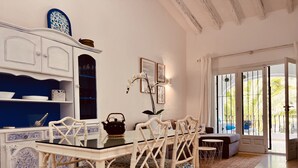 Un comedor con una mesa y sillas blancas, un armario azul y blanco, y vistas al exterior a través de un vidrio.