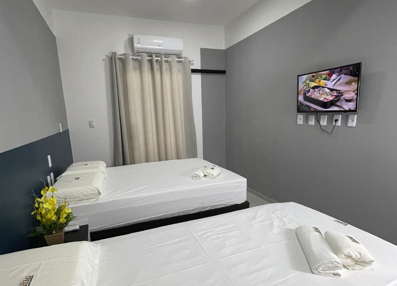 Habitació d'hotel amb dos llits, televisió de pantalla plana penjada a la paret, aire condicionat sobre la finestra i una planta en test amb a la part esquerra.