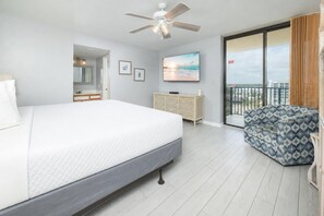 A hotel room with a large bed, a ceiling fan, a television, a dresser, a balcony with a patterned sofa, and a view of the city. - Phoenix IV 4071 — Gulf-Front Bliss (Orange Beach)