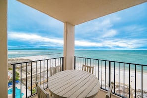 A balcony with a table and chairs overlooking a beach.