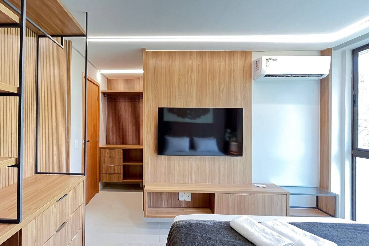 A modern bedroom with a TV mounted on the wall, a bed, a desk, and a wardrobe.