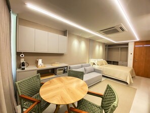 Ein kleines Hotelzimmer mit Küchenzeile, einem Bett, einer Sitzecke mit rundem Tisch und einem Kleiderschrank.