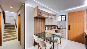 A modern kitchen with a glass dining table, wooden cabinets, and a built-in oven. - Amura Carneiros - Paraíso à Beira-mar (Tamandaré)
