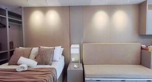 Ein modernes Hotelzimmer mit einem Bett, einem Nachttisch mit Lampe und einer integrierten Sitzbank.