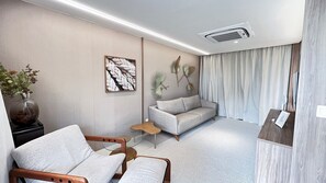 Ein modernes Hotelzimmer mit einer Couch, einem Sessel, einem kleinen Tisch, einer Vase mit Blumen und einem Deckenventilator.