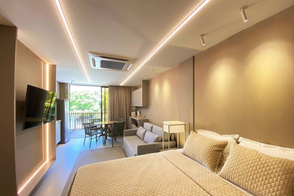 A hotel room with a bed, a TV, a desk, a chair, a sofa, and a balcony.