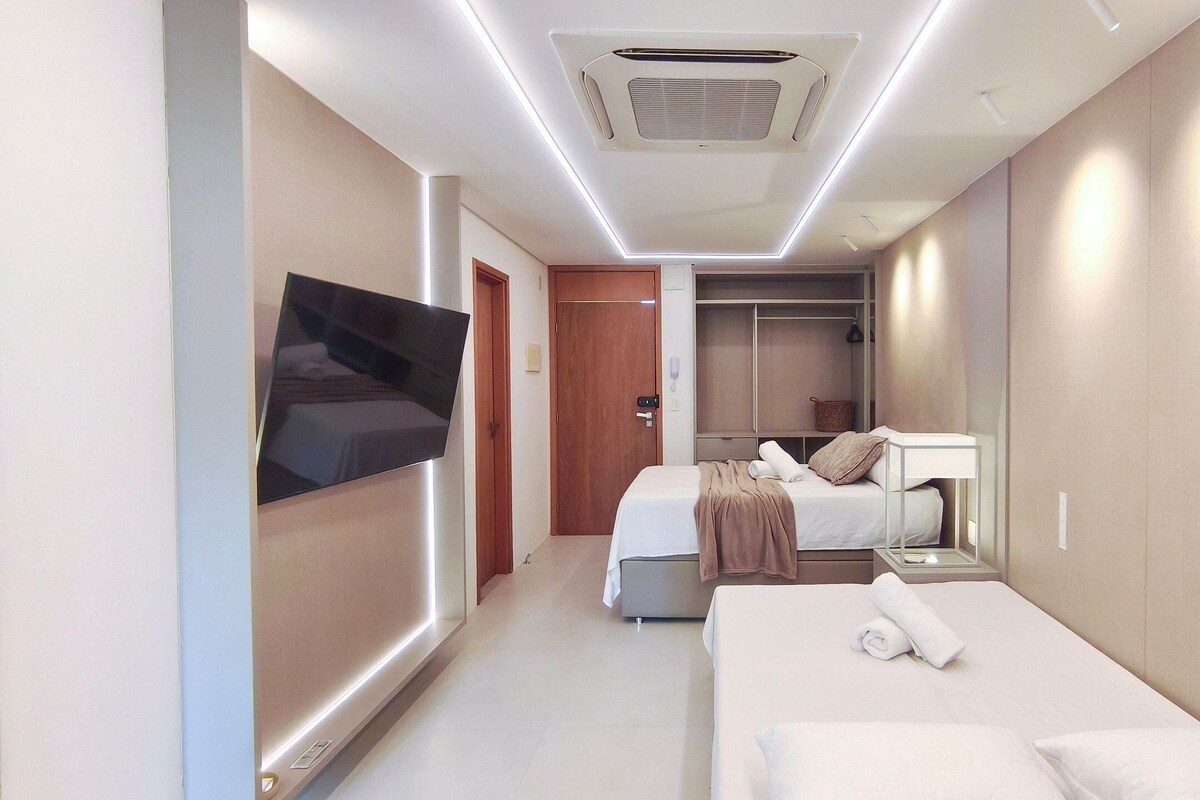 Quarto de hotel com televisão de tela plana, duas camas, closet espaçoso e ar condicionado instalado no teto.