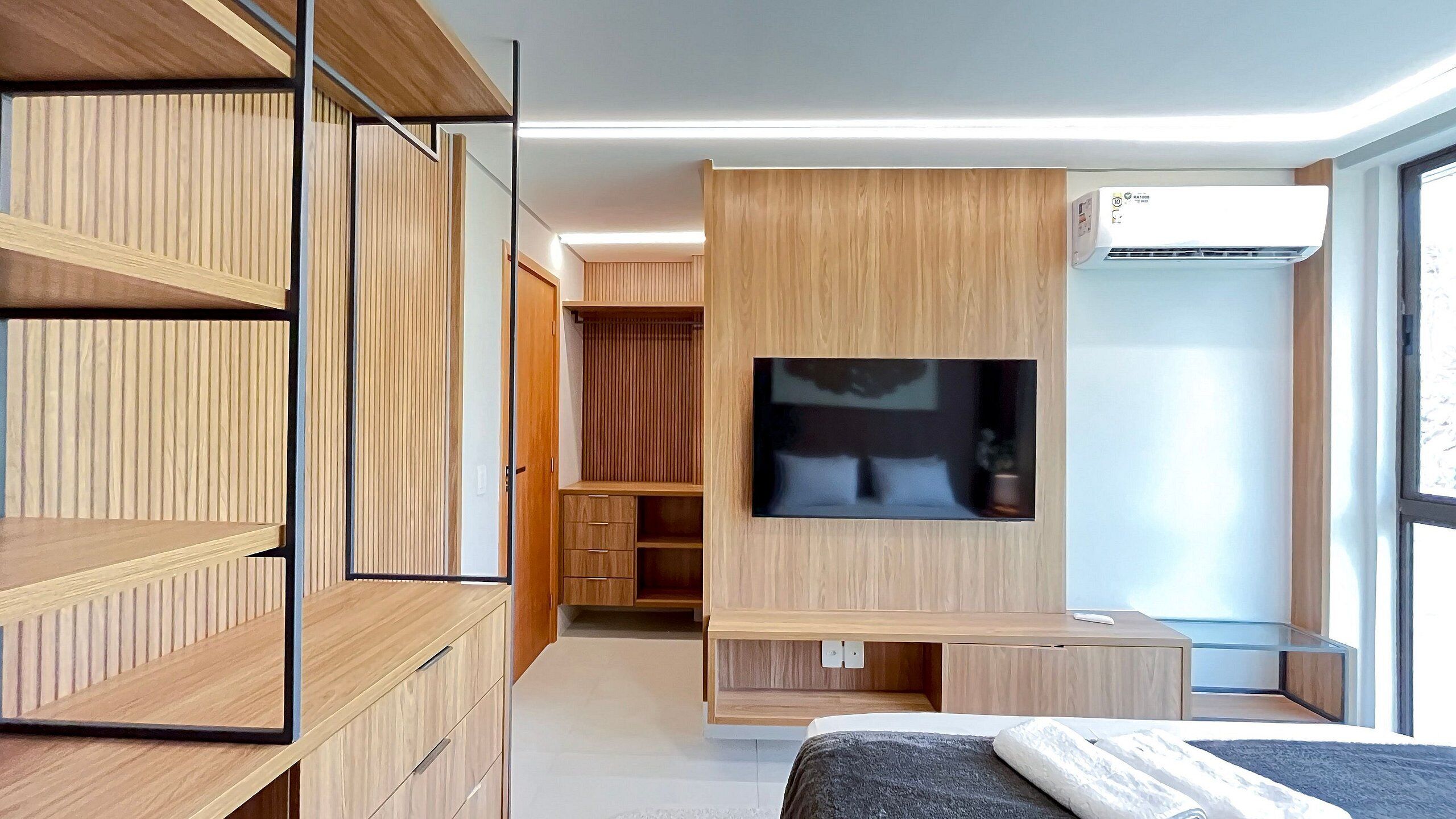 Ein modernes Schlafzimmer mit an der Wand montiertem Fernseher, einem Bett, einem Schreibtisch und einem Kleiderschrank.