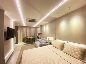 A hotel room with a bed, a sofa, a dining table, and a TV mounted on the wall. - Amura Carneiros - Paraíso à Beira-mar (Tamandaré)