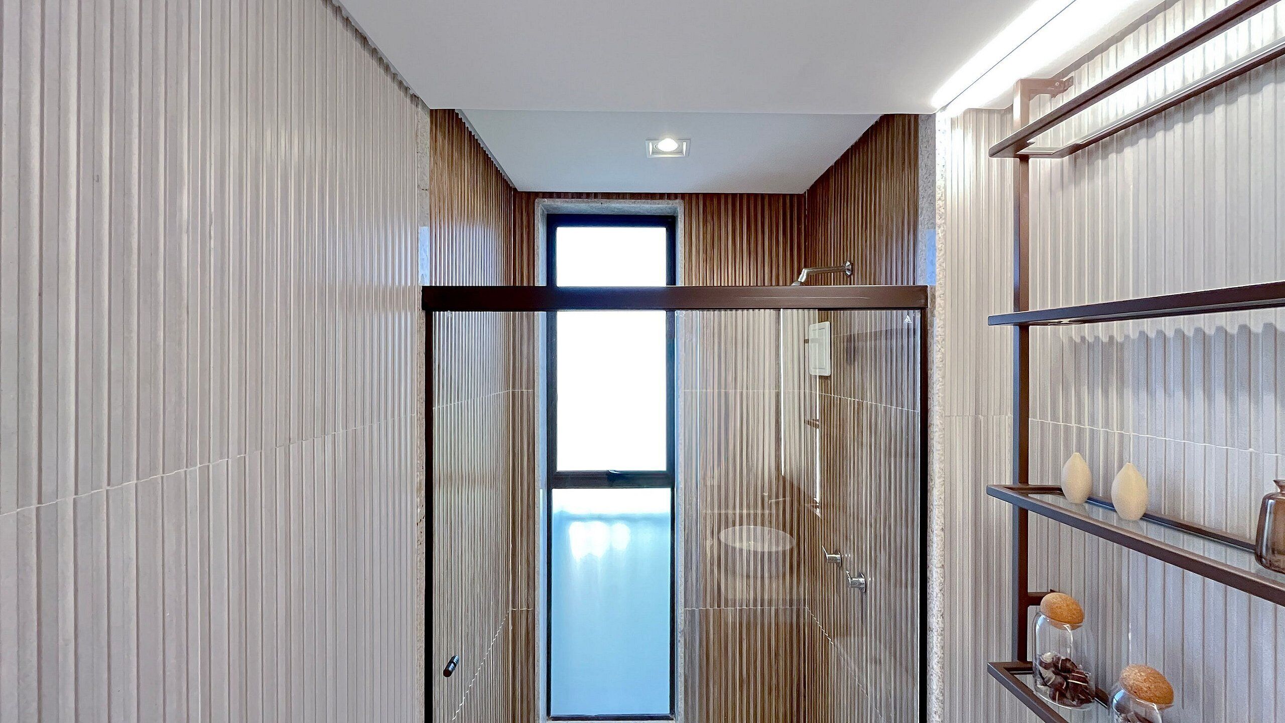 A modern bathroom with a glass shower enclosure, a built-in shelf with toiletries, and a large window providing natural light.