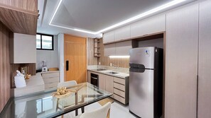 A modern kitchen with a glass dining table, stainless steel appliances, and a built-in oven. - Amura Carneiros - Paraíso à Beira-mar (Tamandaré)