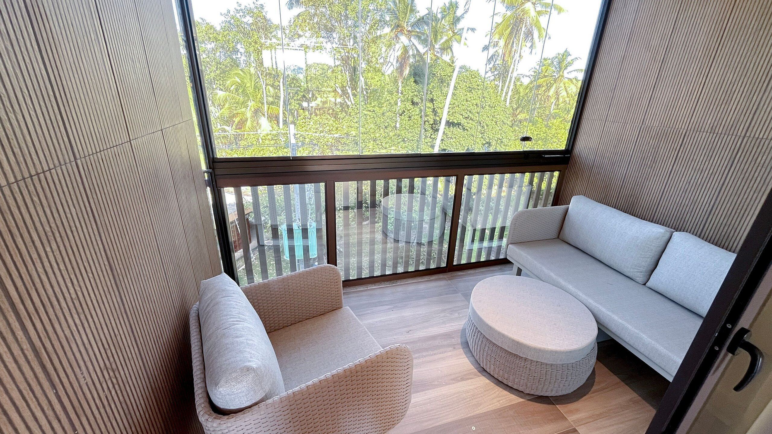 A balcony with a sofa, two chairs, and a round ottoman.