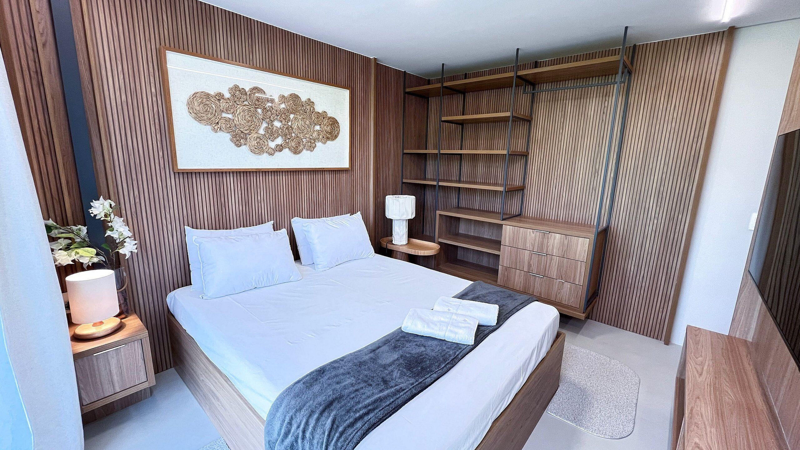 Ein modernes Schlafzimmer mit einem großen Bett, einem Nachttisch, einer Lampe, einem Wanddekor und integrierten Regalen.