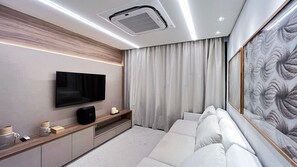 A modern living room with a flat-screen TV, built-in sound system, a sofa, and a large artwork on the wall. - Amura Carneiros - Paraíso à Beira-mar (Tamandaré)