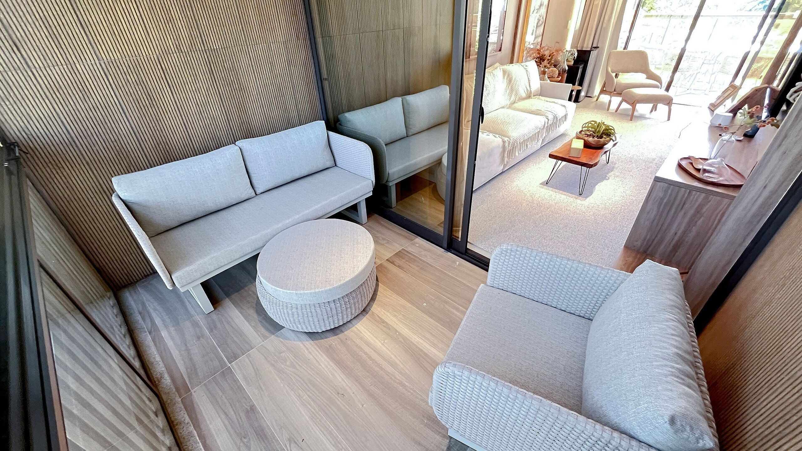 Un salon moderne avec un canapé, un pouf et un fauteuil, une cloison en verre et une vue sur l’extérieur.