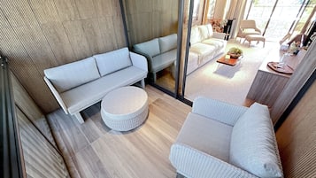 A modern living room with a sofa, ottoman, and armchair, a glass partition, and a view of the outdoors.