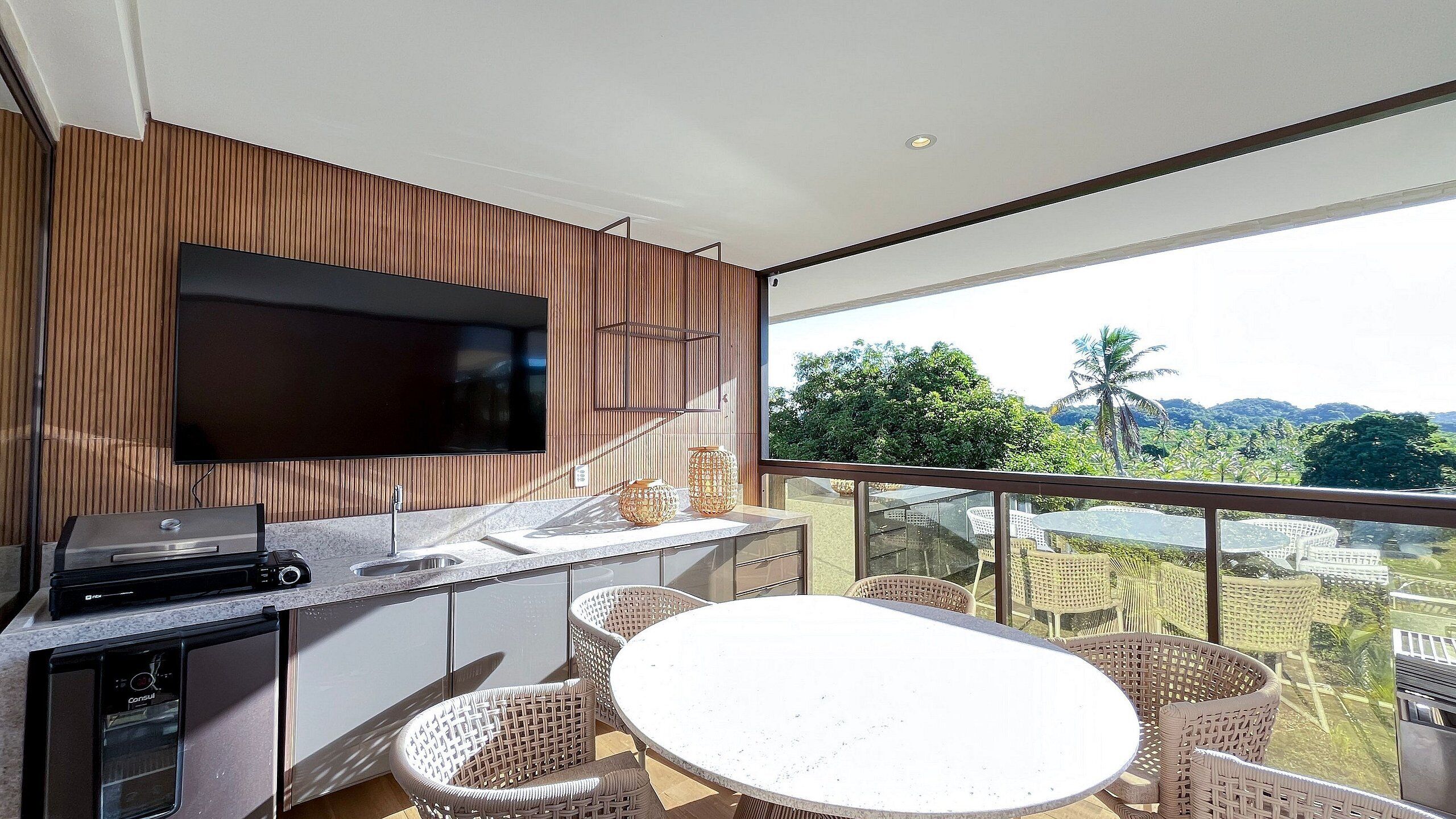 Ein Balkon mit Essbereich, einem Flachbildfernseher und einem Grill.