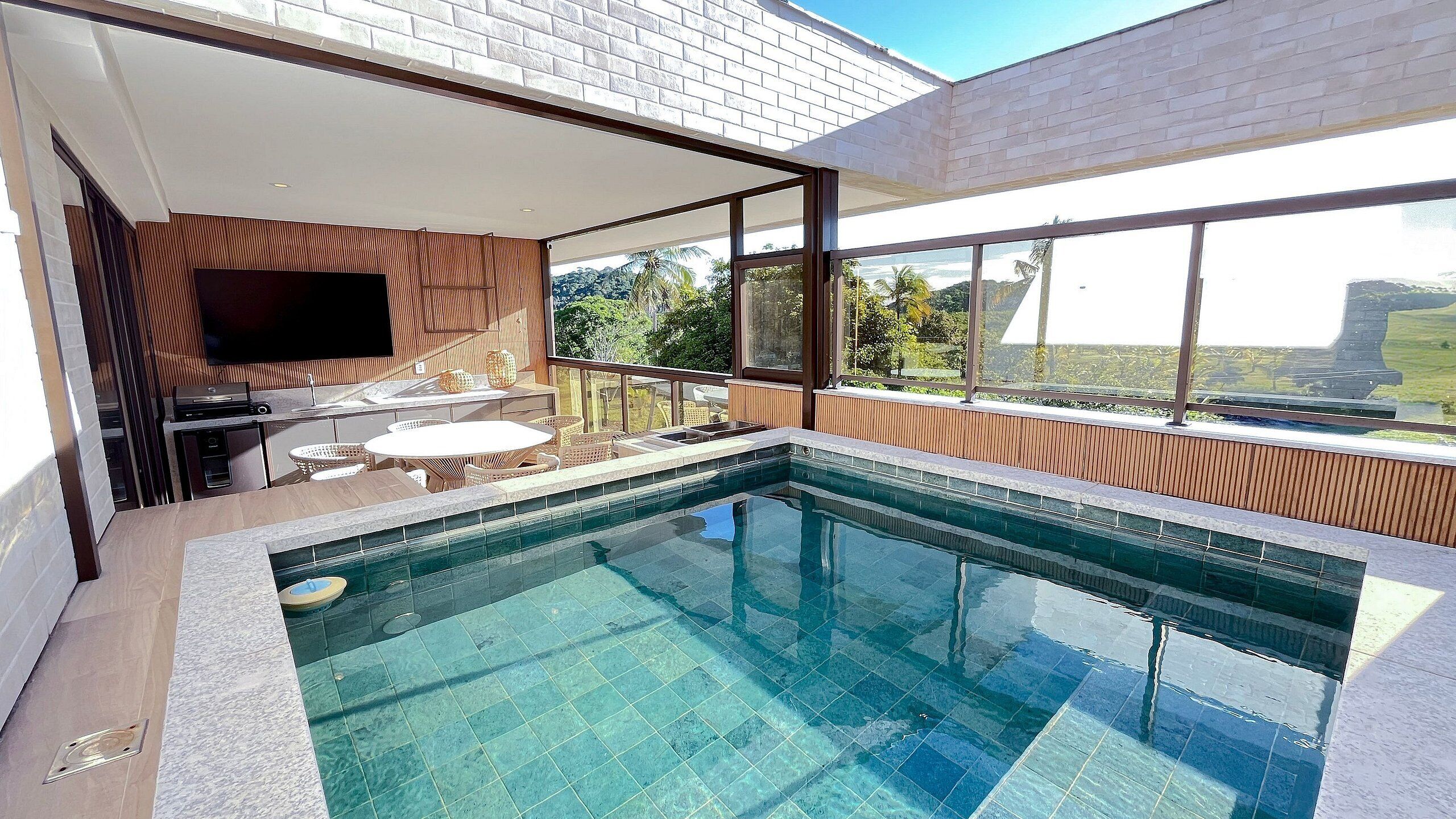 A modern outdoor pool area with a flat roof, a flat-screen TV mounted on the wall, and a view of the surrounding landscape.