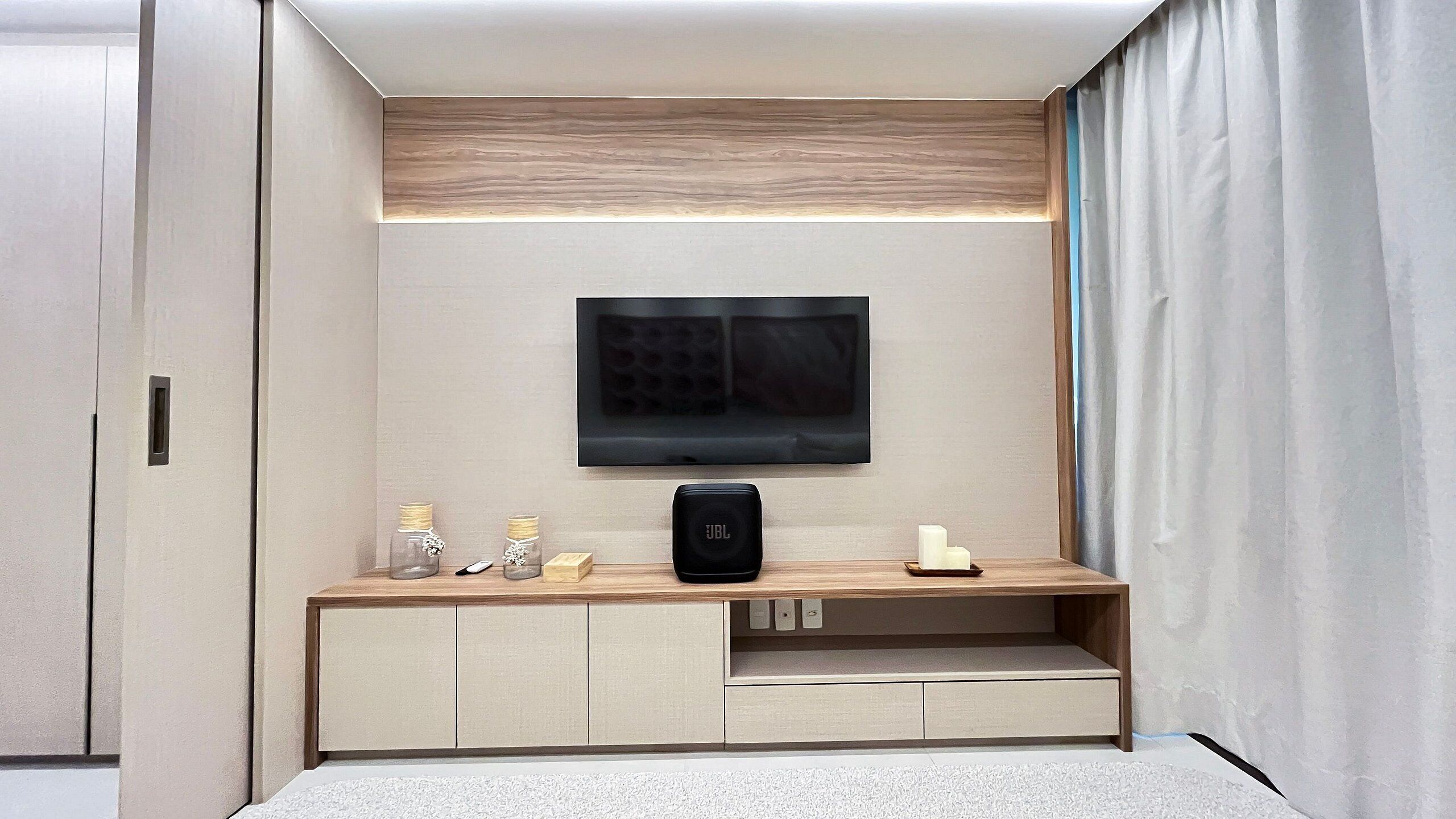A modern room with a flat-screen TV mounted on the wall, a wooden console table with storage, and a carpeted floor.