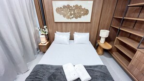 A hotel room with a bed, two bedside tables, a nightstand, a wall-mounted decorative piece, and a staircase.