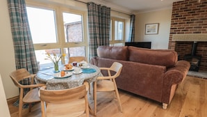 A cozy living room with a brown sofa, wooden chairs, a round table with a polka dot tablecloth, and a fireplace. - Nook Cottage (Alnwick)