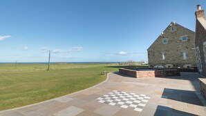 A stone building with a checkered outdoor area and a view of the sea. - Nook Cottage (Alnwick)