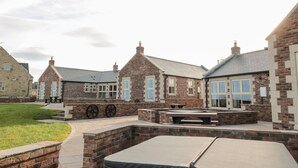 A courtyard with brick buildings, outdoor seating, and a pool area. - Nook Cottage (Alnwick)
