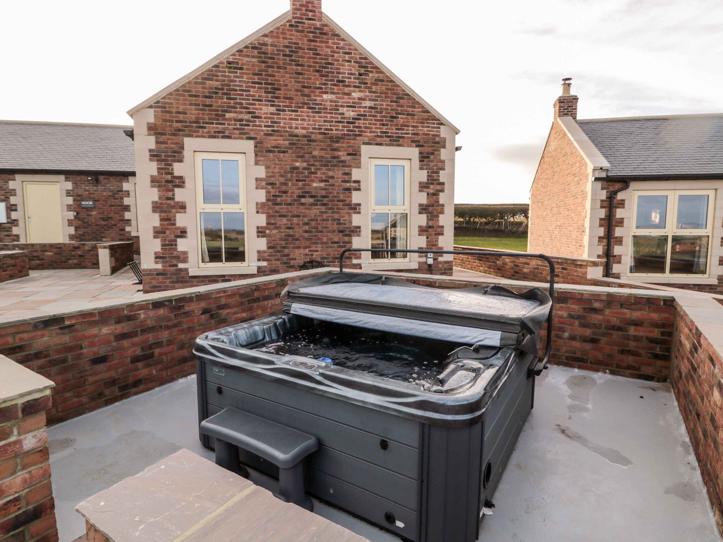 Ein Whirlpool auf einer Terrasse mit Ziegelwänden und Fenstern.