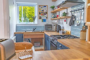 A compact kitchen with a window, a microwave, a stove, and various utensils. - Great getaway for couples at this central Windermere ground floor flat with parking (Windermere)