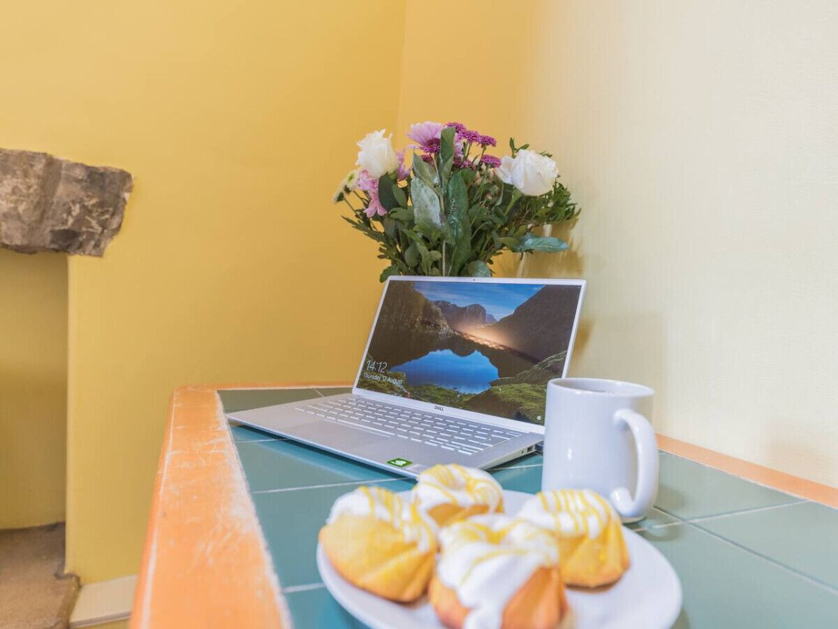 Un ordinateur portable est posé sur une table, à côté d’une tasse blanche et d’une assiette de pâtisseries.
