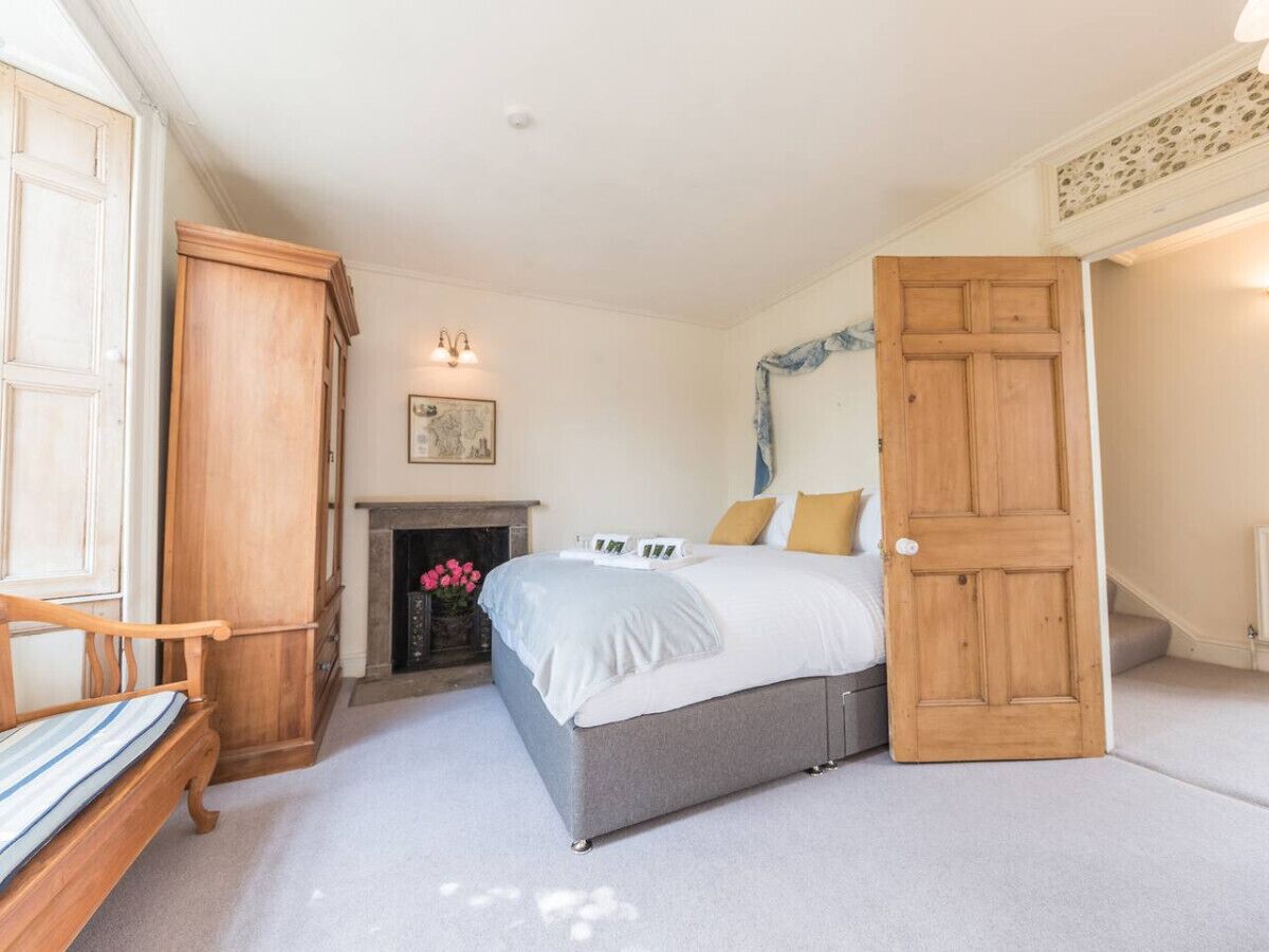 A bedroom with a bed, a wooden wardrobe, a fireplace, and a door leading to another room.
