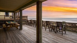 A wooden deck with outdoor seating and a view of the ocean at sunset.