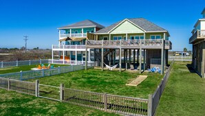 A beachfront property with a two-story house, a covered deck, and a fenced yard with a pool.
