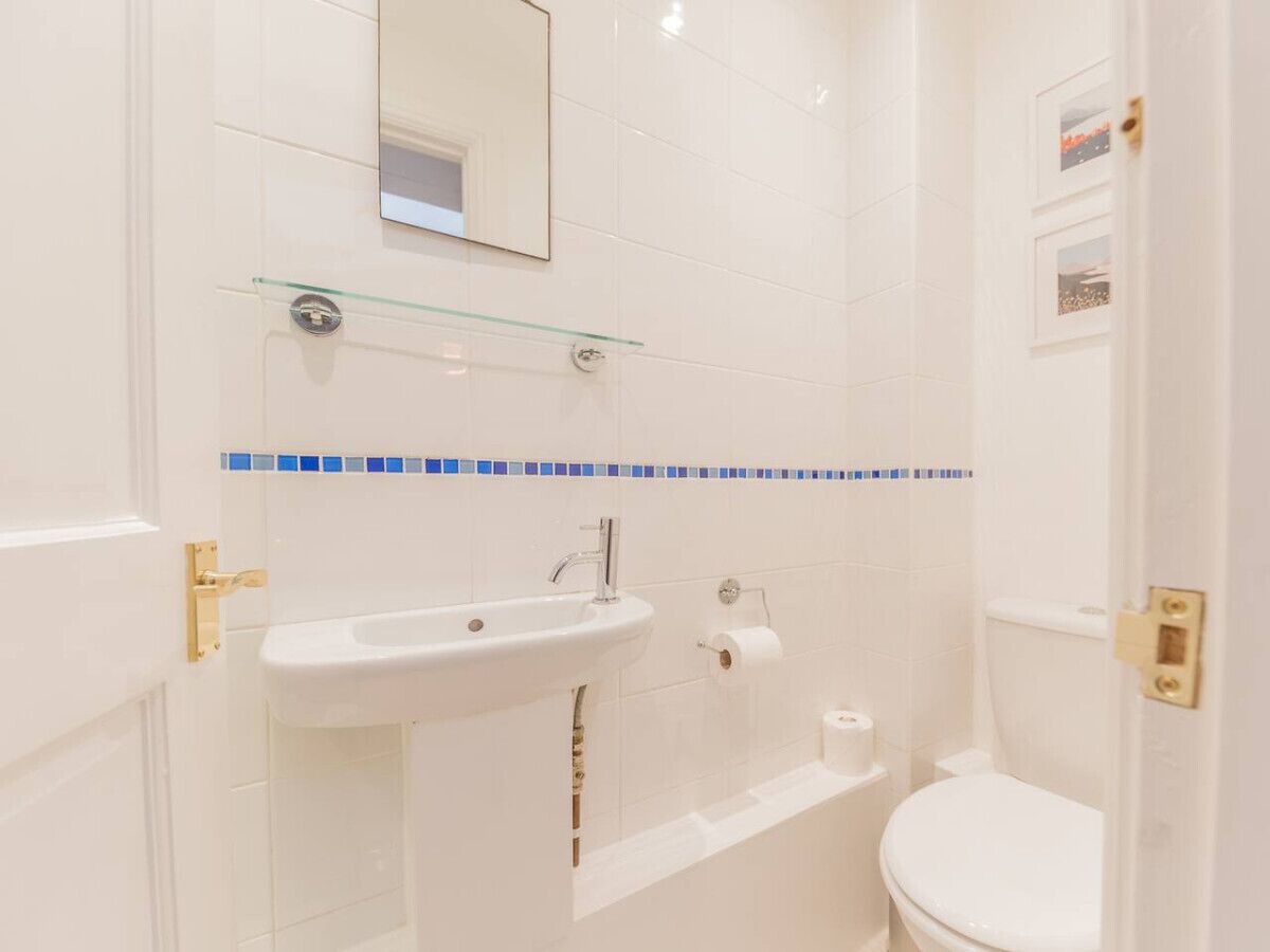 A bathroom with a white sink, a mirror, a toilet, and a glass shelf.