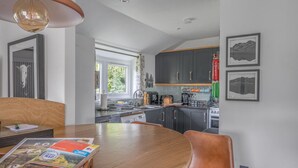 A modern kitchen with dark cabinets, a wooden dining table, and a view of the outdoors. - Romantic getaway, little two bed, two bath barn conversion with amazing views & parking (Ambleside)