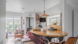 A modern kitchen with a wooden table, bar stools, a TV, and a bookshelf. - Romantic getaway, little two bed, two bath barn conversion with amazing views & parking (Ambleside)