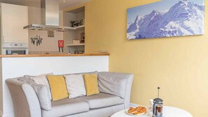 A modern living room with a grey sofa, a white coffee table, and a mountain painting on the wall.