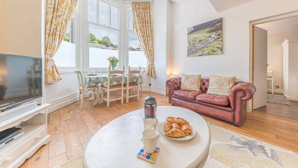 A cozy living room with a TV, a round coffee table with pastries, a red leather sofa, and a painting on the wall.