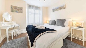 A bedroom with a bed, a vanity with a mirror, a dresser, and artwork on the walls.