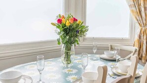 A dining table with a floral tablecloth, a vase of flowers, and diningware.