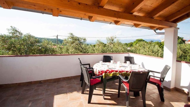 A covered outdoor dining area with a table set for four, surrounded by chairs with red cushions, overlooking a mountainous landscape. - Holiday apartment on the quiet (Vrbnik)