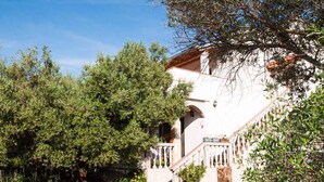 A white building with a staircase, surrounded by lush greenery and potted plants. - Holiday apartment on the quiet (Vrbnik)