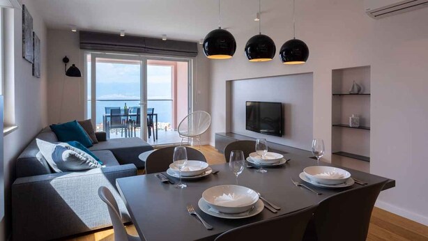 Un moderno comedor con una mesa preparada para cuatro, un sofá y un televisor en la pared.