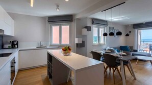 Cocina moderna con una isla central, comedor con sofá y sillas, y ventanas amplias con vistas al exterior.