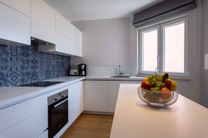 A modern kitchen with white cabinetry, a built-in oven, a coffee maker, and a fruit bowl on the counter.