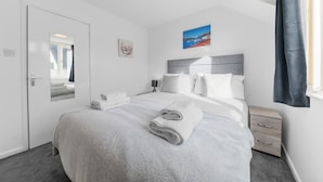A modern hotel room with a neatly made bed, a bedside table, a nightstand, and a window with curtains. - Two minute walk from the World of Beatrix Potter, apartment with parking (Bowness-on-Windermere)